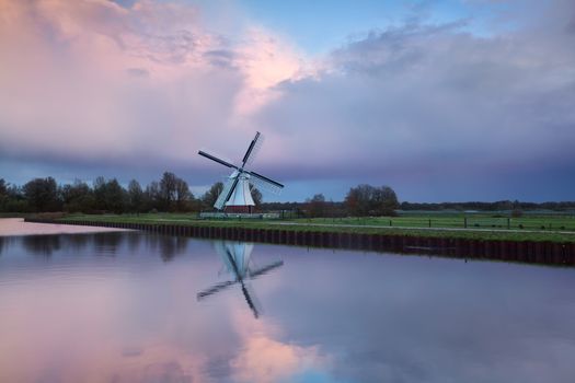 Pink rainy sunset over windmill reflected in river, Holland