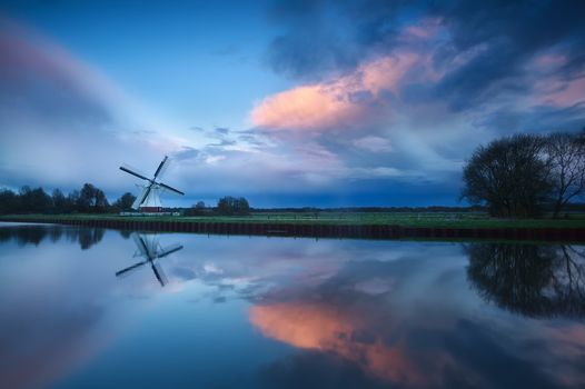 dramatic stormy sunset over Dutch windmill by river, Holland