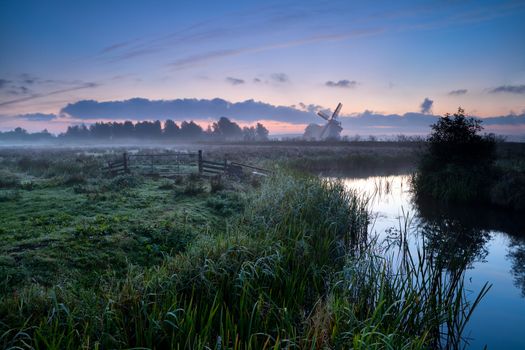 misty morning over Dutch farmland with windmill and river, Groningen, Netherlands