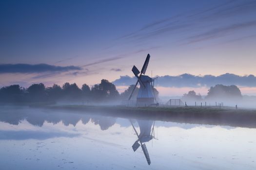 Dutch windmill reflected in river in sunrise fog, Groningen, Netherlands