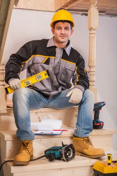 young contractor sitting on wooden ladder holding constructionh level