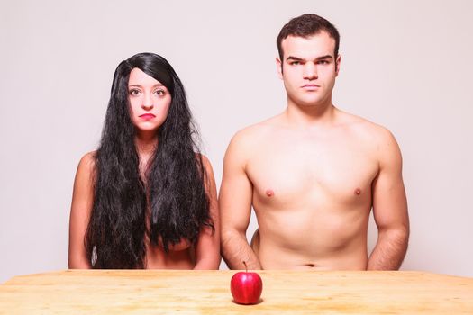 The apple of temptation sitting on a wooden table in front of a naked couple conceptual of a modern day Adam and Eve