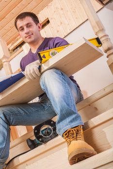 a young worker siiting on step of ladder and holding wooen board with tools on legs