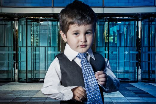 Professional, child dressed businessman with hands in his tie and skyscrapers in the background