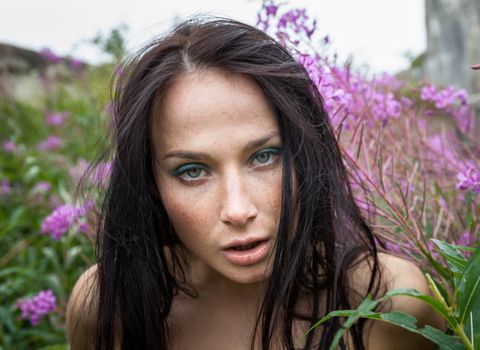 Beautiful freckled girl among the flowers and old concrete wall background