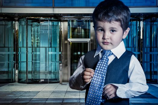 Professional child dressed businessman with hands in his tie and skyscrapers in the background