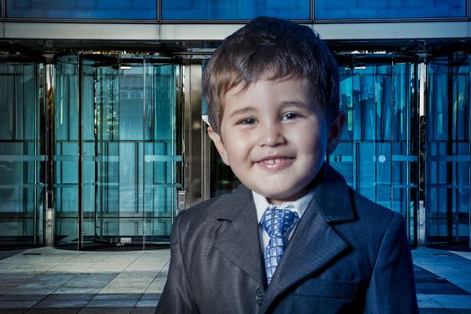 Happy child dressed businessman with hands in his tie and skyscrapers in the background