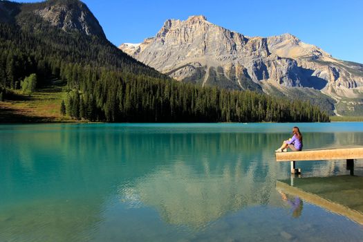 Young woman sitting on a pier at Emerald Lake, Yoho National Park, British Columbia, Canada