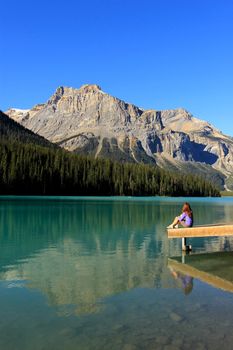 Young woman sitting on a pier at Emerald Lake, Yoho National Park, British Columbia, Canada