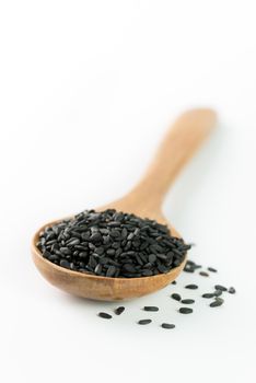 Heap of black sesame on wooden spoon on white background