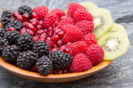 Bowl of fresh exotic tropical fruit with colourful neat rows of blackberries, pomegranate seeds, raspberries and thinly sliced kiwifruit on a stone counter for a delicious healthy vegetarian dessert