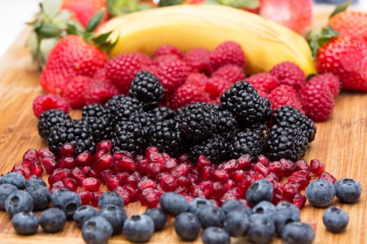 Assorted freshly washed fruit in the kitchen arranged on a wooden countertop in colourful rows with blueberries, blackberries, pomegranate seeds, raspberries, strawberries and a fresh banana