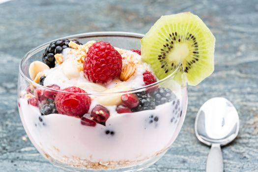 Closeup of a glass of delicous frozen berry parfait containing blackberries raspberries, pomegranate seeds and almonds, garnished with a slice of kiwifruit
