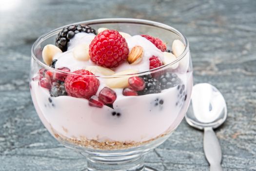 Glass of creamy rich berry parfait topped with almonds and made with raspberries, blackberries and pomegranate seeds served on a stone countertop