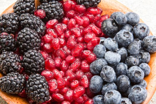 Closeup of juicy mixed berries and succulent pomegranate seeds in a wooden bowl with blackberries and blueberries for a healthy dessert rich in antioxidants