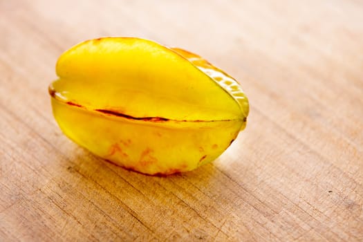Single whole crisp juicy ripe yellow carambola or star fruit on a wooden cutting board with copyspace