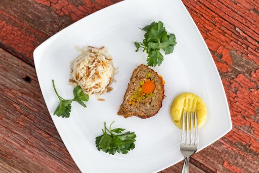 Vegetable stuffed meatloaf served with rice pilaf and mashed potato, garnished with parsley on picnic table