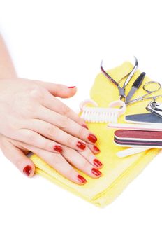 Woman's Hands with Bright Red Manicure and Heap of  with Nail File, Scissors, Toe Divider and Other Accessories closeup on Yellow Napkin on white background