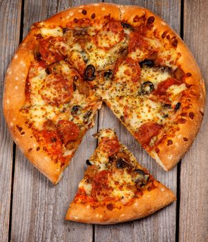 Freshly Baked Pepperoni Pizza with Black Olives and Spices and Slice on Rustic Wooden background