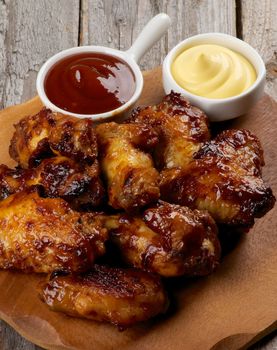 Arrangement of Chicken Legs and Wings Barbecue with Ketchup and Cheese Sauces on Wooden Plate closeup