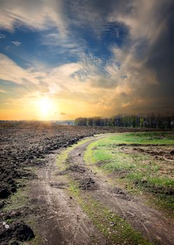 Sunset and country road through the plowed field