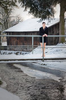 Young woman in mini costume, standing in pumps in the winter on a bridge over the brook