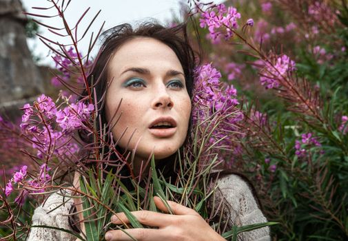 Portrait of beautiful freckled girl among the flowers. Intentional color shift
