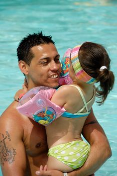 Father and daughter in pool giving eachother a hug.