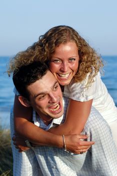 A happy woman and man in love at beach. The young man is carrying his girlfriend on the back of his shoulders.