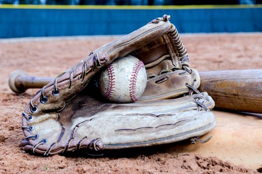 Baseball bat, glove, and ball on base on field.  