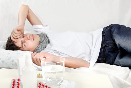Sad and Sick Young Man lying on the Bed with Pills on foreground
