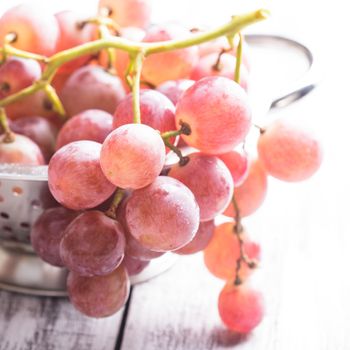 Big red grapes in  colander on the wood background