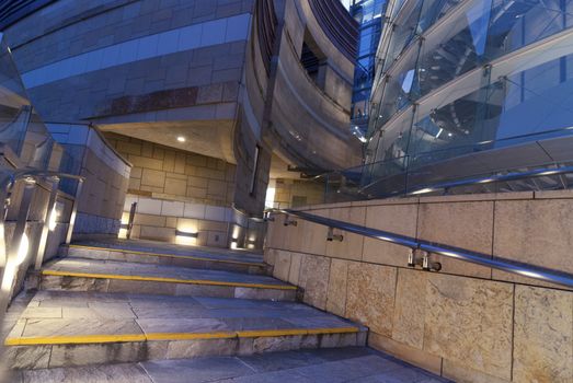 modern architecture fragment with spiral stone stairs and blue glass wall