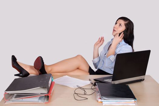 Young female office worker with feet on desk phone and explains