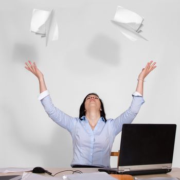 Young woman sitting at table with laptop and throws out the paper in the air