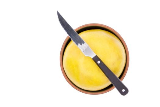 Kitchen knife on a ripe yellow grapefruit or pomelo fitted tightly into a small bowl ready to be cut and prepared for breakfast, isolated on white with copypace, overhead view