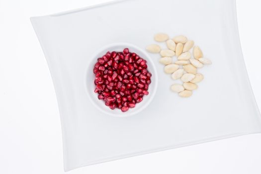 Bowl of fresh ripe red pomegranate seeds with whole peeled or blanched almonds served on a white plate for a healthy nutritious snack or appetizer, overhead view