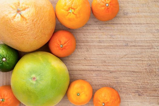 Mixed citrus fruit border over a textured wooden background with copyspace with a crescent shaped arrangement of clementines, nectariines, tangerines, lime, orange and grapefruit