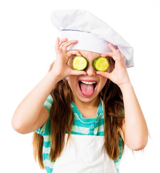 little girl in chef hat with cucumber slices on the eyes shows tongue on a white background
