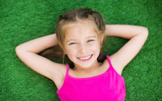 Little smiling cute girl lying on green grass