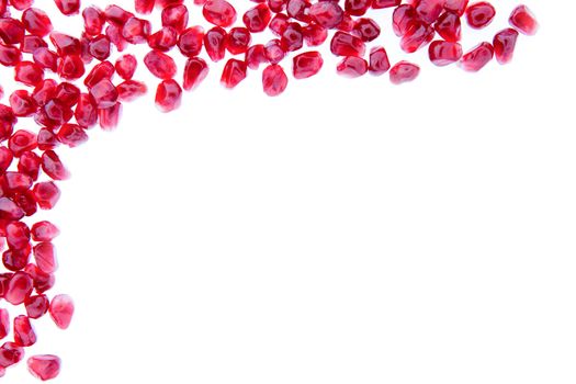 Border of fresh ripe pomegranate seeds arranged in the top left corner and isolated over a white background with copyspace