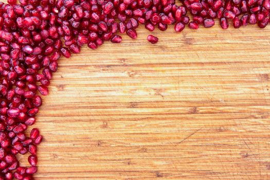 Border of fresh ripe red pomegranate seed on a textured wood background arranged in a pile in the top left corner with ample copyspace for your text or menu
