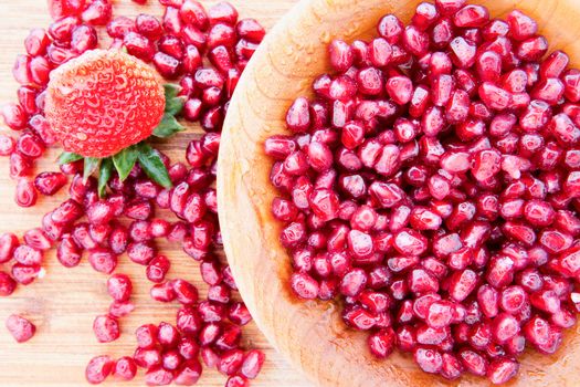 Wooden bowl of fresh pomegranate seeds rich in vitamins and antioxidants and used in Ayuverda medicine with a single ripe red strawberry with a green stalk