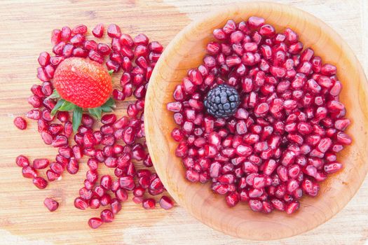 Fresh ripe juicy red pomegranate seeds rich in vitamin k and used extensuly in Ayuverda medicine with a single strawberry and blackberry in a bowl ready for a healthy snack or dessert