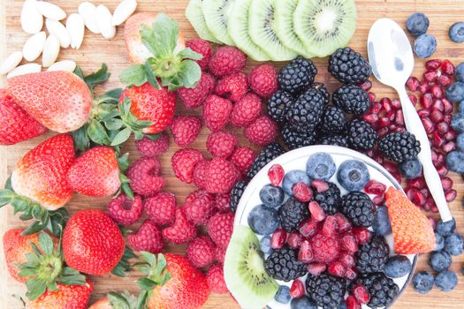 Preparing a delicious healthy berry fruit salad with assorted fresh fruit on the counter including strawberries, raspberries, blackberries, blueberries, pomegranate and kiwifruit with almonds