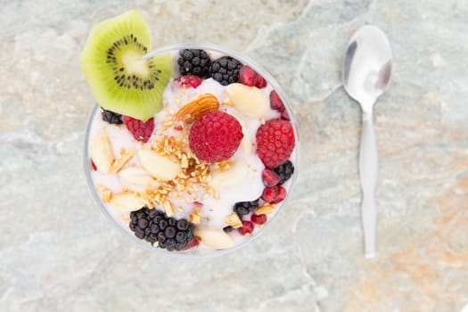 Overhead view of a frozen parfait dessert topped with fresh raspberries, blackberries and almond nuts and garnished with a slice of tropical kiwifruit