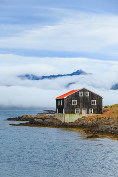 Lonely Black Wooden House at coastline in East Iceland. Vertical view.