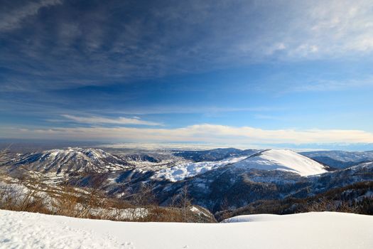 Candid off-piste ski slope in scenic background of mountain peaks, valleys and plain. Piedmont, Italian Alps