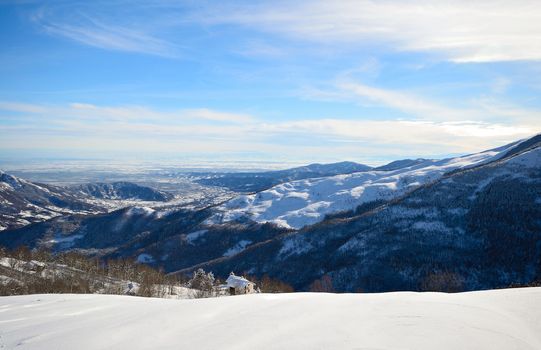 Candid off-piste ski slope in scenic background of mountain peaks, valleys and plain. Piedmont, Italian Alps