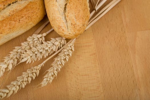 Freshly baked traditional roll on wooden table with ears of wheat grain